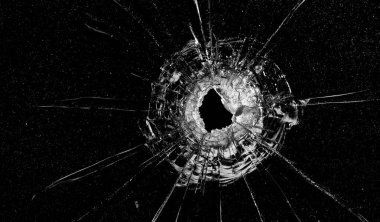 Cracks in the glass on a black background. A bullet hole in a window on a dark background.