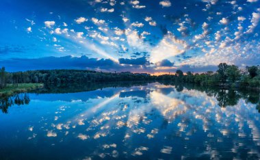 Dawn over the meadow next to the river. A wonderful summer landscape. Green trees and blue water. Drone view, natural background.