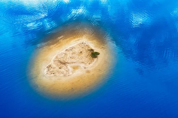 A small island in the ocean, clean sand, and blue water, drone view. Reflection of clouds in water.
