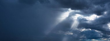 The beginning of a powerful thunderstorm. Dark rain clouds and sun rays.
