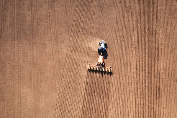 A tractor with a seeder on the field drone view, the spring season of the sowing campaign.