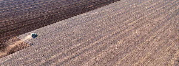 A tractor in the field cultivates the soil before the start of the sowing campaign. Drone view. Agricultural work in the field in early spring. The concept of agriculture.