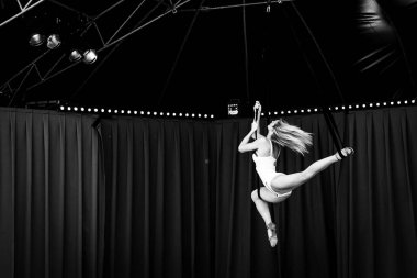 Bir sirk göstericisinin güzel bir pozda asılı duran siyah beyaz portresi. Çadırdaki ipleri kullanarak. Esnek sanatçı yetenekli bir sanatçıdır ve dengeli bir performansı vardır..