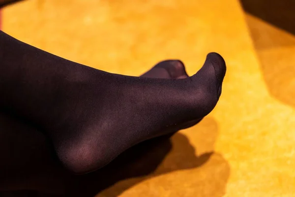 A portrait of the crossed feet of a girl wearing black opaque nylon pantyhose or stockings with a reinforced toe while sitting in a couch, curving her toes a little. Great under a dress or skirt.