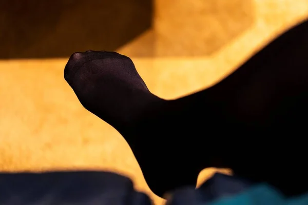 A portrait of a foot of a girl wearing black nylon opaque pantyhose or stockings with a reinforced toe while sitting in a couch. Great under a dress or skirt.