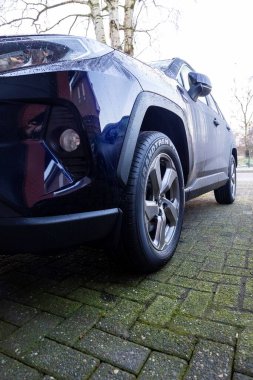 Brecht, Belgium - 21 january 2022: A portrait of the right headlight of a dark blue hybrid toyota rav4 car parked on a driveway. The vehicle can drive electrically and on fossil fuel. clipart