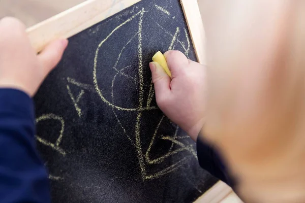 涂鸦幼儿在黑板上涂鸦 乱画或画一点的特写肖像那孩子正在黑板上写字 手里拿着一支黄色的粉笔 — 图库照片