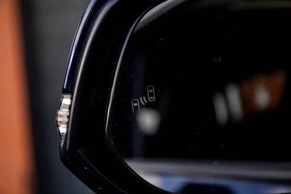 A close up portrait of the emblem of the pedestrian and other vehicle detection safety feature in a sideview mirror of a car, which lights up when there is somekind of danger of having an accident.