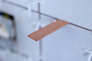 İki kiremit arasında ortak boşluk olarak kullanılan ahşap bir uzay aracının yakın plan portresi aynı zamanda plastik beyaz uzaylılarla döşenmiş bir duvardaki kavşak için doğru mesafenin tutulduğundan emin olmak için..
