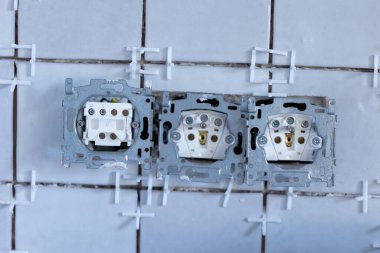 Bir ışık düğmesi ve iki elektrik prizinin portresi. Koruyucu kapakları olmayan, yeni döşenmiş bir duvarda, hala bağlantı noktalarında beyaz plastik eklem boşlukları olan..