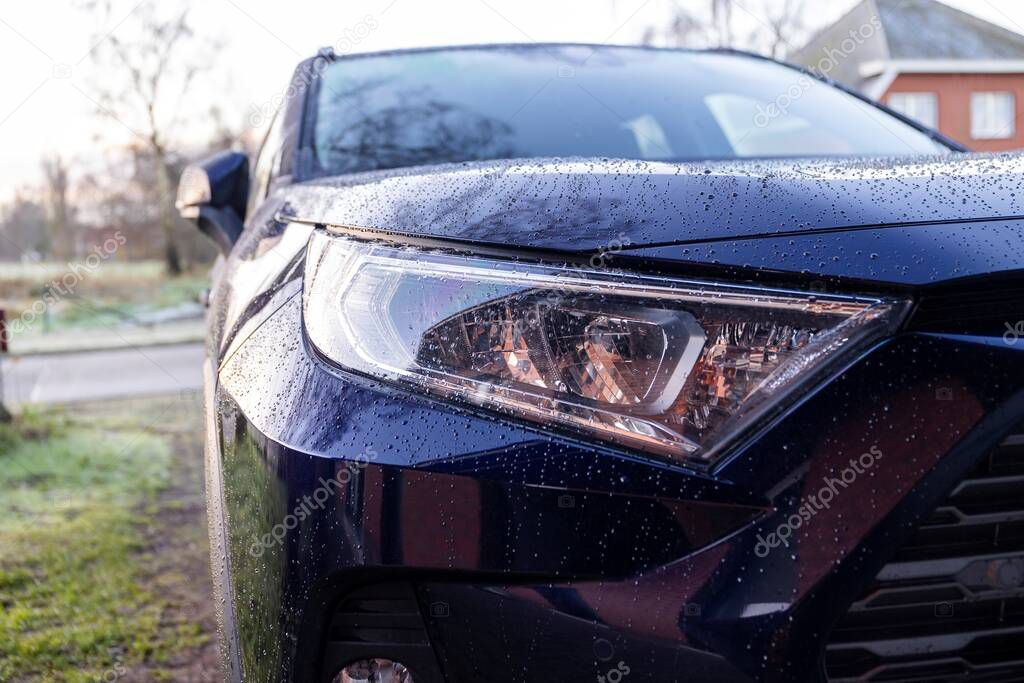 A close up portrait of the left headlight of a dark blue hybrid toyota rav4 car parked on a driveway. The vehicle can drive electrically and on fossil fuel.