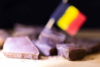 Tahta bir yüzeyde duran lezzetli, kahverengi Belçika çikolatasının, aralarında bulanık bir Belçika bayrağının bulunduğu kaba kesilmiş parlak bir portresi..