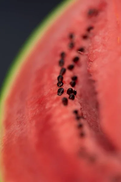 A vertical closeup portrait of the black seeds sitting in the pink red pulp of a cut slice of green watermelon. The piece of fruit is ready to be eaten and is very nutritious.