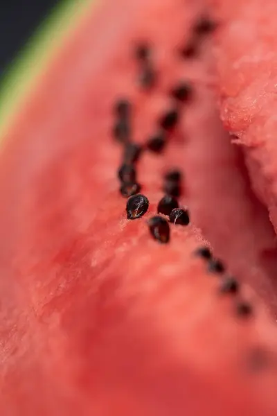 A vertical closeup portrait of the black seeds sitting in the pink red pulp of a cut slice of watermelon. The piece of fruit is ready to be eaten and is very nutritious.