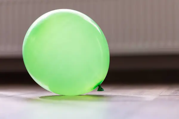 A closeup portrait of a green balloon lying on a floor in a house. The decoration item is blown up and ready to be played with and used to celebrate a birthday party or anniversary.
