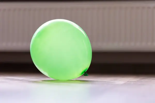 A portrait of a green balloon lying on a living room floor in a house. The decoration item is blown up and ready to be played with and used to celebrate a birthday party or anniversary.