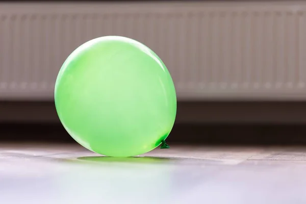 A portrait of a green balloon lying on a floor in a house. The decorative item is blown up and ready to be played with and used to celebrate a birthday party or anniversary.