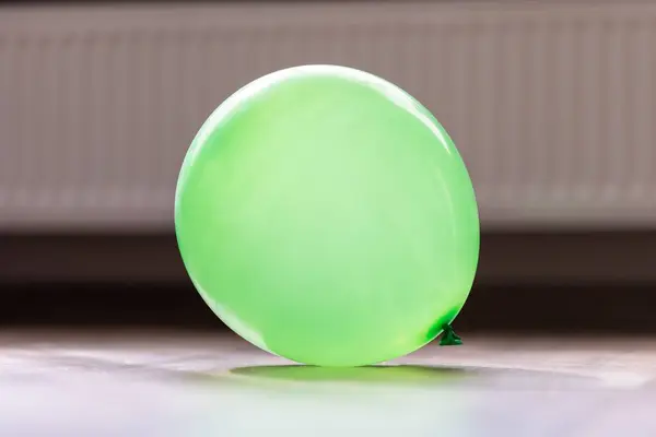 A portrait of a green balloon lying on a floor in a house. The decoration item is blown up and ready to be played with by children or adults and use to celebrate a birthday party or anniversary.