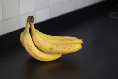 Siyah bir mutfak tezgahında duran kahverengi benekli sarı muz demetinin yakın plan portresi. Lezzetli enerji veren yemekler yemek için hazır ve spor etkinliğinden önce ideal..