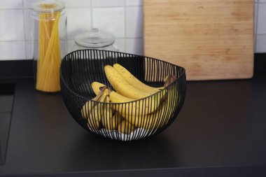 Siyah mutfak tezgahındaki dekoratif siyah metal bir kasede yatan bir grup muzun portresi. Sağlıklı enerji veren yiyecekler spordan önce yenmeye hazır..