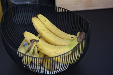 Siyah mutfak tezgahındaki dekoratif siyah metal bir kasede duran bir grup muzun yakın plan portresi. Sağlıklı enerji veren yiyecekler spordan önce yenmeye hazır..