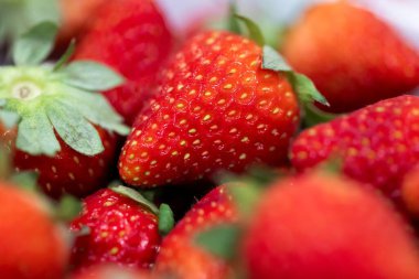Beyaz bir kasenin içinde yeşil başlıklı lezzetli ve taze çileklerin yakın plan portresi. Lezzetli meyve yenmeye hazır..