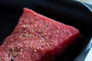 Kızartma tavasında pişirilen ya da hazırlanan kırmızı çiğ bifteğin çeşnili portresi. Lezzetli etin üzerinde mükemmel bir akşam yemeği ya da yemek için biber ve tuz var..