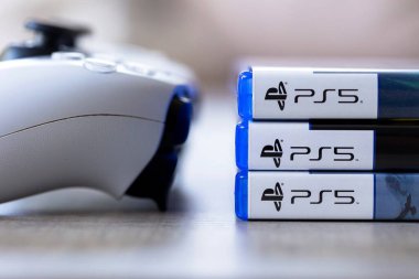 Brecht, Belçika - 3 Ekim 2024: üzerinde ps5 logosu olan oyun kasalarının yanında duran bir Playstation 5 kontrolörünün yakın çekimi. Her şey oyun konsolunda bir video oyunu oynamaya hazır..