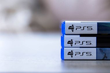 Brecht, Belçika - 3 Ekim 2024: Üst üste istiflenmiş 3 Playstation 5 veya PS5 oyun çantalarının ön yakın plan portresi, açılmaya ve yanlarında açık alanla oynamaya hazır.