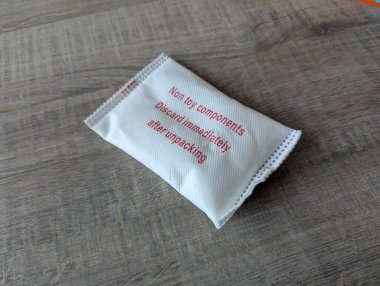 Close-up of a silica gel packet on a wooden table, used for dehumidifying and keeping package contents dry, preventing moisture damage and spoilage. clipart