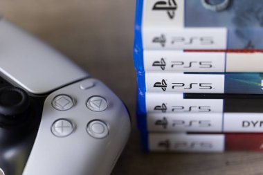 Brecht, Belçika - 18 Nisan 2025: Sony Playstation 5 video oyun çantaları ya da kablosuz PS5 kontrolörünün yanındaki tahta masada duran kutular. PS5 oyunlarının yığını çoklu türdür.