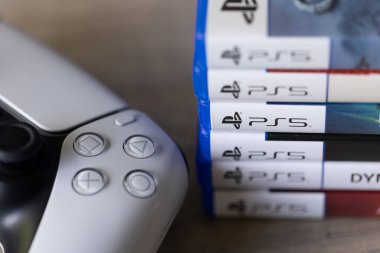 Brecht, Belçika - 18 Nisan 2025: Sony Playstation 5 video oyun kutuları veya kablosuz PS5 kontrolörünün yanındaki tahta bir masanın üzerinde duran çantalar. Bir konsol oyunu oynamaya hazır.