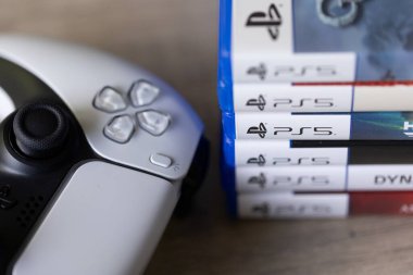 Brecht, Belçika - 18 Nisan 2025: PS5 kablosuz kontrolörünün yanındaki ahşap bir masada duran bir yığın sony playstation 5 video oyun kutusu veya kutu. Bir konsol oyunu oynamaya hazır.
