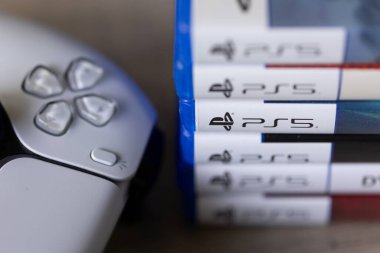Brecht, Belçika - 18 Nisan 2025: PS5 kablosuz kontrolörünün yanındaki ahşap bir masanın üzerinde duran bir yığın sony playstation 5 oyun çantasının yakın plan portresi. Bir konsol oyunu oynamaya hazır.