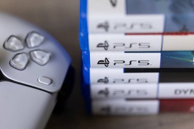 Brecht, Belçika - 18 Nisan 2025: Orijinal beyaz bir PS5 kablosuz kontrolörünün yanındaki Sony Playstation 5 oyun çantalarının veya kutularının yakın plan portresi. Bir konsol oyunu oynamaya hazır.