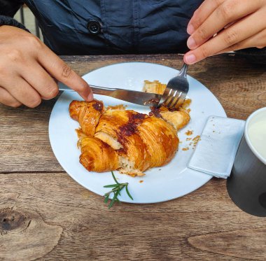 Kruvasan beyaz bir tabakta. Yemek yiyebilmek için çatal ve bıçakla parçalara ayrıldılar.