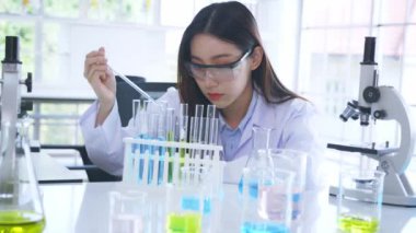 Eczane laboratuvarında çalışan genç bayan Asyalı tıp araştırmacısı tüpteki kimyasalları mikroskop ve test tüpü gibi aletlerle karıştırırken. Yüksek kalite 4k görüntü