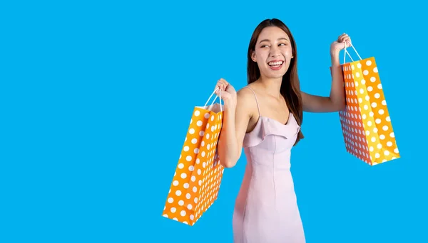 笑容满面的亚洲女购物者一边走一边看着相机 手里拿着一堆购物袋 穿着蓝色背景衣服的漂亮女孩 半身长在演播室拍摄 — 图库照片