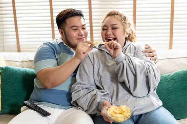 Young Asian chubby couple watching tv series and movie on the couch in living room. Man and woman enjoying a fun time together at home. People laughing and smiling together