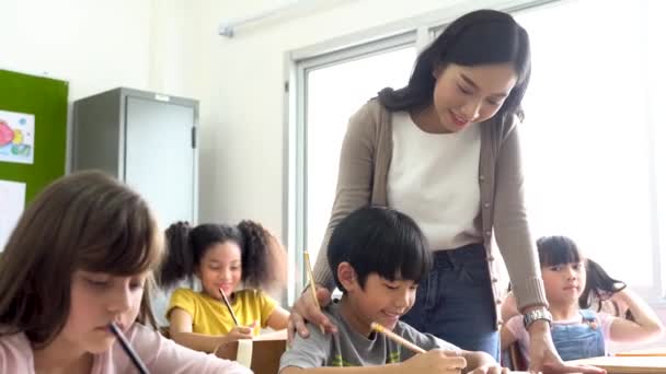 教室で学生を支援するアジアの学校の先生 学校で執筆 サポート ケアで少年を助ける若い女性 — ストック動画