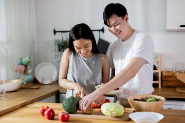 Aşık Asyalı bir çift mutfakta sağlıklı bir salata yapıyor. Gülümseyen mutlu sevgili, evde yemek pişirmekten zevk alıyor..