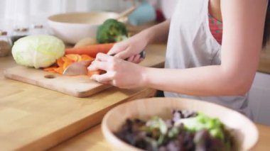 Young Asian woman in fitness sportswear slicing and cutting raw vegetables such as cabbage and carrot in kitchen at home. Vegetarian making a salad.