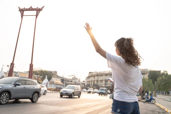 忙しい街の通りでタクシーを呼ぶ手を上げている若いアジアの女性 スマートフォン経由でタクシーサービスアプリケーションを使用して10代の観光客 コピースペース付き — ストック写真