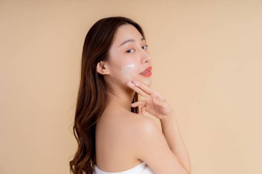 Stüdyoda yüzüne beyaz krem sürmüş sağlıklı bir yüz derisi olan Asyalı genç bir kızın yakın plan portresi. Cilt bakımı ve cilt bakımı kavramı.