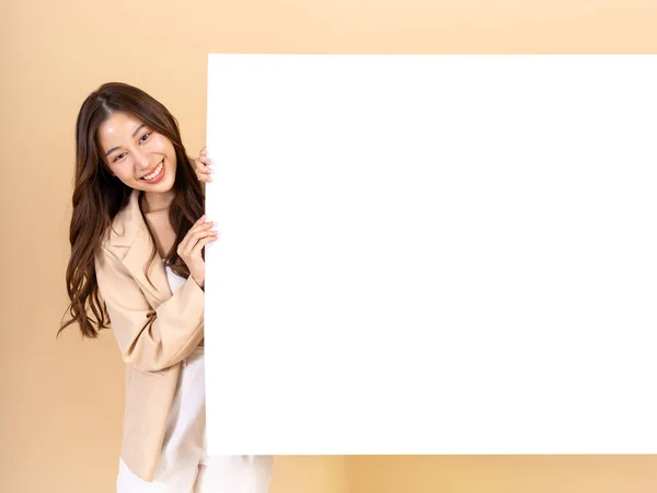 在米色背景下 年轻的亚洲女人拿着一块巨大的空白空白广告牌 上面有复制空间 用于广告和营销推广 — 图库照片