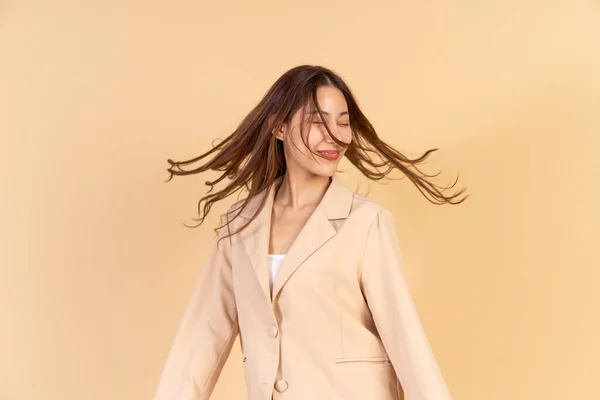 Young Asian happy smiling woman in casual business suit having flying hair in motion isolated over beige background.