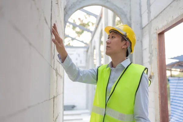 Asian engineer in uniform at construction site while checking and inspecting concrete material for house building. Professional engineering manager working on structure building at workplace.