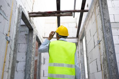 İnşaat alanında çelik yelek giymiş, kasklı bir mühendis. İş yerindeki yapı inşaatında çalışan genç profesyonel ustabaşı.