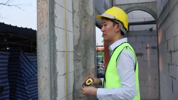 高精度を測定するために測定テープを使用して建設現場で制服やヘルメットをエンジニアリングの若いアジアのエンジニア 職場における構造物の構築に取り組む30代の専門家 — ストック動画