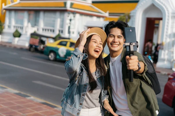 stock image Portrait of Asian man and woman couple travelers in relationship taking a selfie video call in front of buddhist temple on street in Bangkok, Thailand, Southeast Asia - carefree and happiness concept